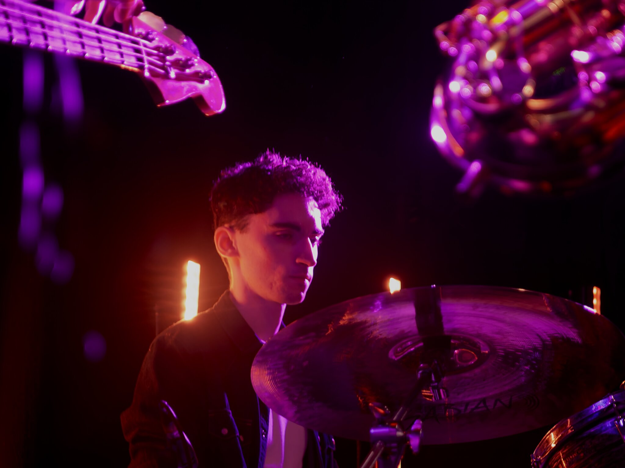 Drummer mid-set behind the cymbals under purple lights